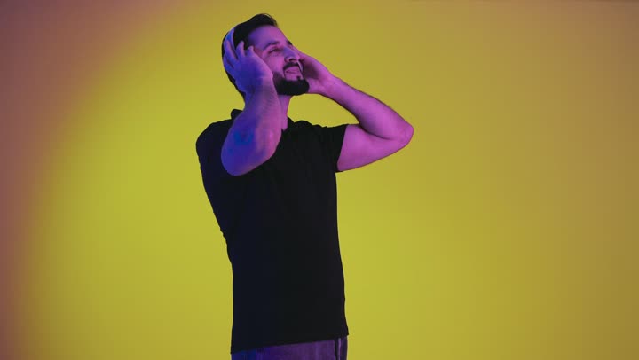 Artistic singing talents, an Arab Gulf Emirati man holding and holding his headphone, gestures and facial expressions indicating happiness and integration with the song, a portrait of a Saudi young man wearing casual clothes listening to music, a recording of a singing audio clip, a yellow background