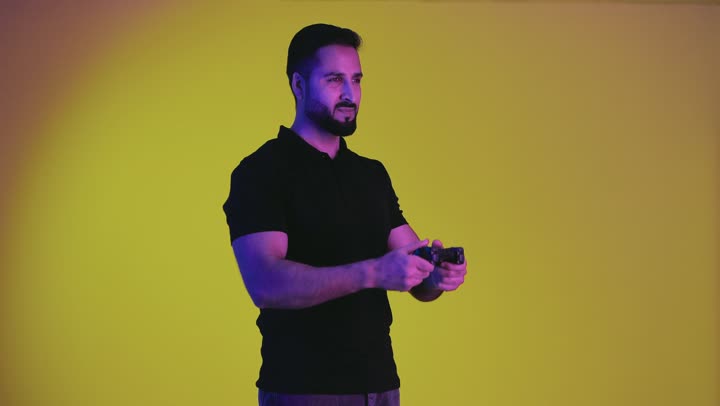 A young Saudi Arabian Gulf man holding a joystick and playing video games with gestures and expressions indicating victory and happiness, a portrait of an Emirati man wearing casual clothes feeling fun and entertainment with video games, playing the entertaining PlayStation, yellow background