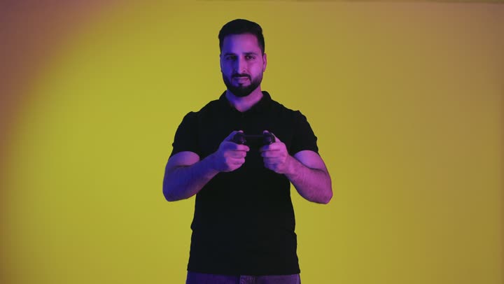 بورتريه لشاب عربي خليجي سعودي يمسك بيده عصا التحكم و يلعب ألعاب الفيديو بإيماءات و تعابير تدل على الفوز والسعادة، المتعة والتسلية بألعاب الفيديو، رجل اماراتي يرتدي الزي الكاجوال يقوم بالفوز في ألعاب الفيديو، المتعة والتسلية بألعاب الفيديو، خلفيه صفراء