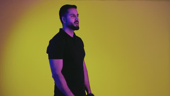 Recording a singing audio clip, an Emirati man presenting segments, programs, and giving lectures, having a good time performing vocal performances, a portrait of an Arab Emirati Gulf young man wearing casual clothes holding a microphone in his hand and singing with gestures of happiness and integration, yellow background