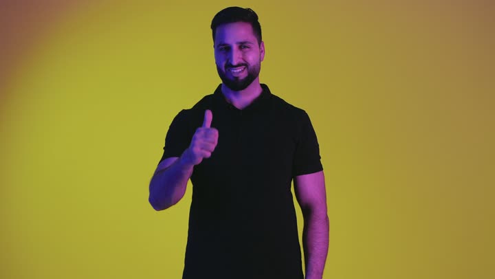 Looking at the camera with an expression of happiness and pleasure, a sign of quality and excellence, a portrait of a young Arab Gulf Emirati man wearing casual clothes raising his thumb up with gestures of admiration and satisfaction, the concept of approval and acceptance, a smiling Saudi man achieving something, yellow background