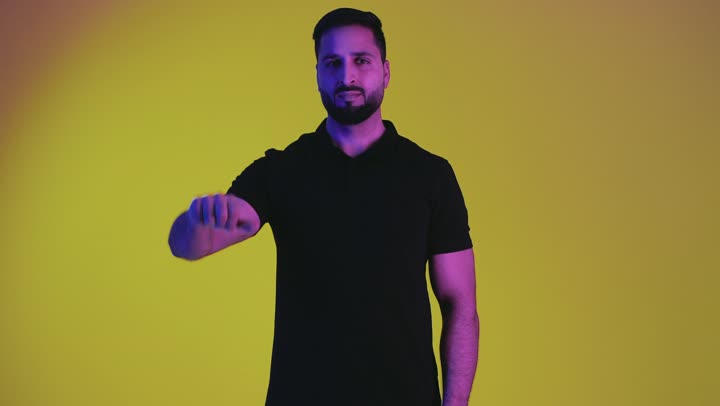 الشعور بعدم القبول والرضا، تعابير الرفض والتقييم السلبي، القلق والفشل في أمر ما، بورتريه لرجل عربي خليجي اماراتي يرتدي الزي الكاجوال يشير بابهامه للأسفل بإيماءات الإنزعاج، شاب سعودي يرفض شئ ما، خلفية صفراء