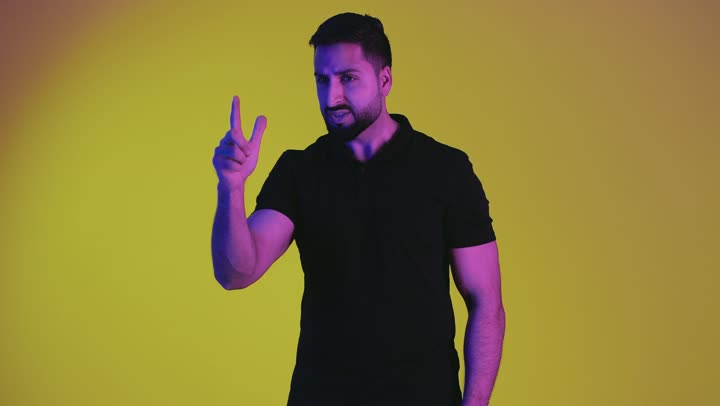 Feeling annoyed and wanting revenge, asking to stop making mistakes, hand gestures indicating reprimand, accusation and blame, portrait of a young Arab Gulf Emirati man wearing casual clothes raising his index finger forward angrily and frowning, a Saudi man blaming someone, yellow background