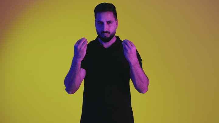 Command to be calm and stand still, request to be patient and slow down, stop doing something, refusal and non-submission, a Saudi young man forbidding progress and the importance of leaving a safe distance, portrait of an Arab Gulf Emirati man wearing casual clothes raising his hand up with gestures of anger and seriousness, yellow background