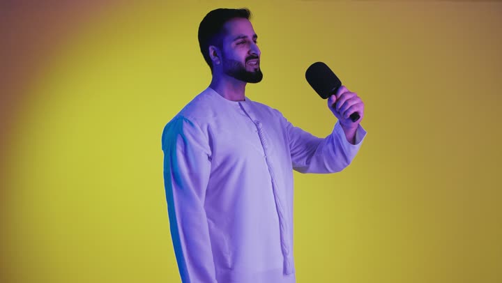 Gestures of integration and interaction with singing, presenting theatrical performances and entertainment segments, a picture of an Emirati Gulf Arab man wearing the Emirati kandura, holding a microphone and singing enthusiastically, recording a singing audio clip, yellow background.
