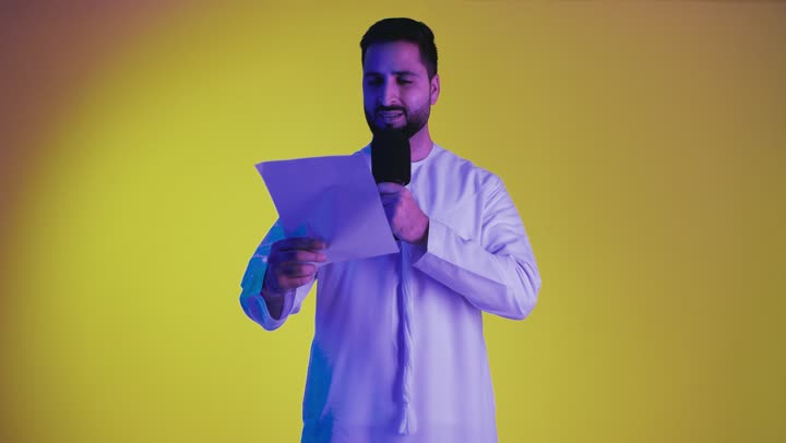 Presenting theatrical performances and entertainment segments, gestures of integration and interaction with singing, a picture of an Emirati Gulf Arab man wearing the Emirati kandura, holding a microphone and singing enthusiastically, recording a singing audio clip, yellow background.