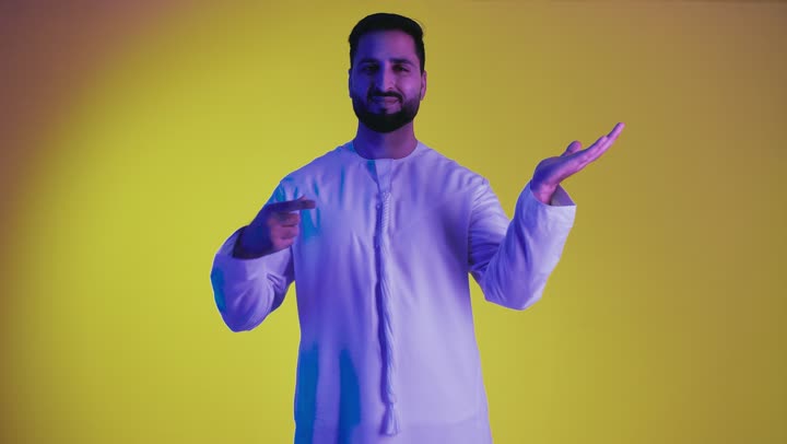 رفع شيء معين, تعابير حمل و إمساك عنصر محدد ، مفهوم الاناقة و الاهتمام بالمظهر الخارجي, تصوير لشاب عربي خليجي اماراتي يرتدي الكندورة يفتح يديه لعرض عناصر هولوجرامية ثلاثية الأبعاد،  خلفية صفراء .