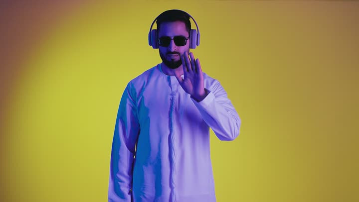 النهي والزجر والانصات، طلب التوقف عن الكلام والصمت، وضع اصبع السبابة أمام الفم بإيماءات الجدية، الأمر بالصمت التام، تصوير لرجل عربي خليجي اماراتي يرتدي الكندورة ونظاره سوداء ينظر للكاميرا بإيماءات الغضب، خلفية صفراء.