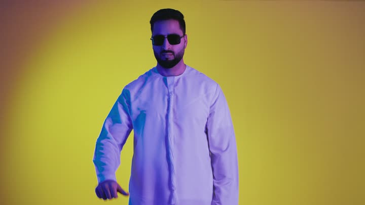 Feeling annoyed by something, gestures of dislike and negative evaluation, hand gestures indicating rejection, non-acceptance, and failure, a picture of an Emirati Gulf Arab man wearing a kandura pointing his thumb down, yellow background.