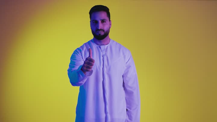 Expressing admiration and appreciation, excellence and full marks, raising hands with signs of quality and acceptance, feeling satisfied and appreciative, a picture of an Emirati Gulf Arab man wearing a kandura looking at the camera with gestures of happiness and pleasure, yellow background.