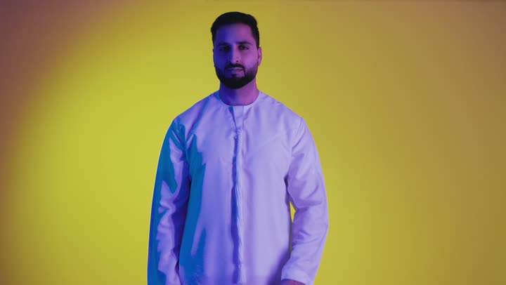 The concept of refusal and abstention, gestures asking to stop and not approach, a picture of an Arab Gulf Emirati man wearing a kandura, standing straight with his hands raised, looking at the camera with a firm expression, full body length, yellow background.