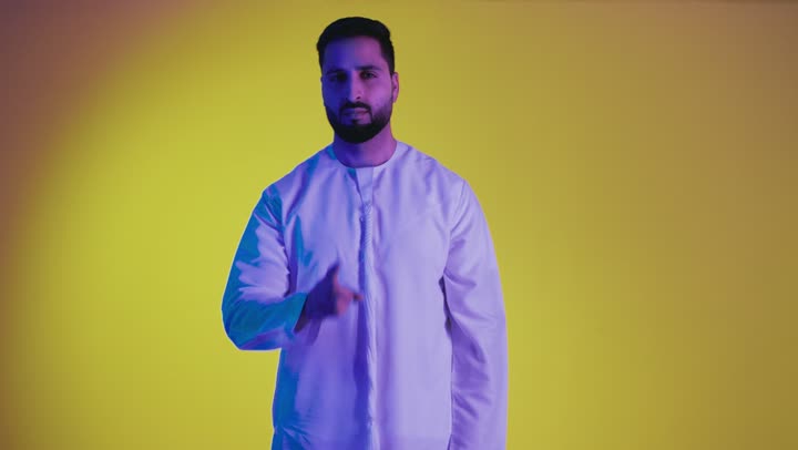 A request to stop talking and be silent, a prohibition, a warning, and listening, placing the index finger in front of the mouth with a serious gesture, an order for complete silence, a picture of an Arab Gulf Emirati man wearing a kandura looking at the camera with angry gestures, full body, yellow background.