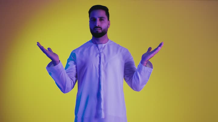 Questioning, astonishment, and inquiry about something, ambiguity and lack of clarity, questioning about a specific topic, a picture of an Arab Gulf Emirati man wearing a kandura raising his hands upwards with gestures of confusion and lack of knowledge, yellow background.