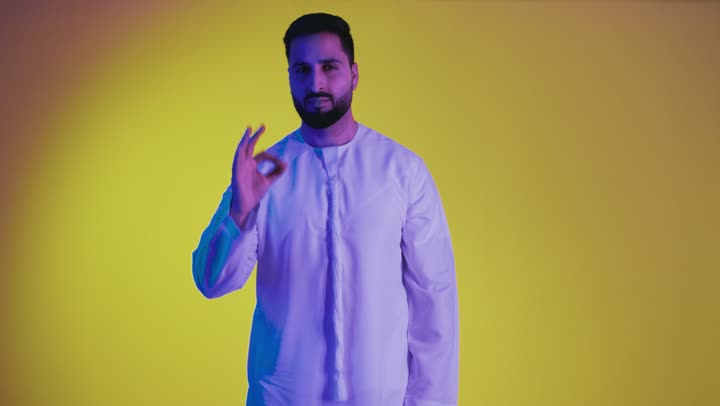 Feeling satisfied and pleased, excellence and full marks, raising hand with signs of quality and acceptance, expressing admiration and appreciation, a picture of an Emirati Gulf Arab man wearing a kandura looking at the camera with gestures of happiness and pleasure, full body, yellow background.