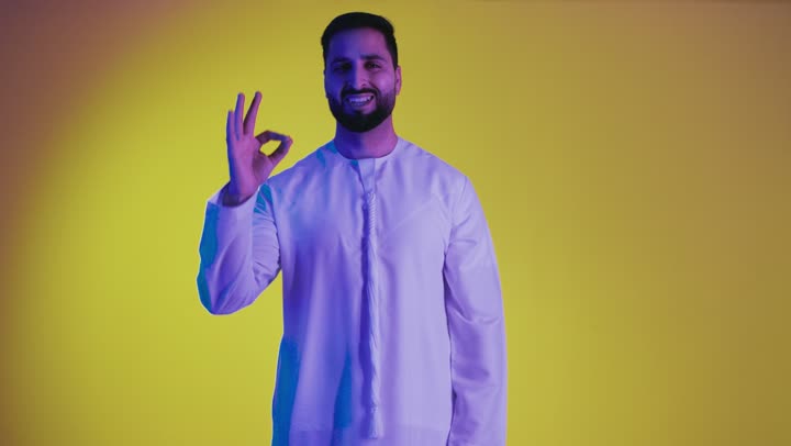 Excellence and full marks, raising hands with signs of quality and acceptance, expressing admiration and appreciation, feeling satisfied and pleased, a picture of an Emirati Gulf Arab man wearing a kandura looking at the camera with gestures of happiness and pleasure, full body, yellow background.