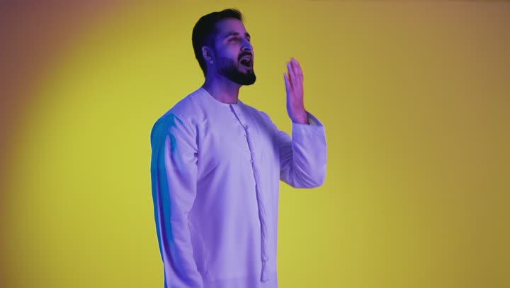 Feeling sleepy and needing to sleep, the need to take some rest and relaxation, gestures of tiredness and exhaustion, a picture of an Arab Gulf Emirati man wearing a kandura, putting his hand over his mouth and yawning, yellow background.