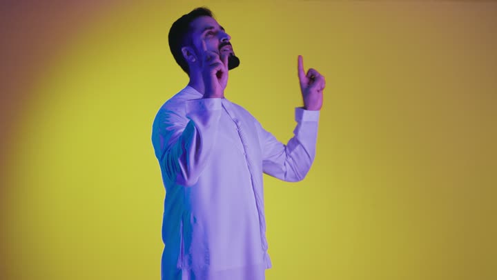 Indicating the location of an item, pointing and explaining something, specifying a specific location, a picture of an Emirati Gulf Arab man wearing a kandura pointing his index finger upwards, yellow background.