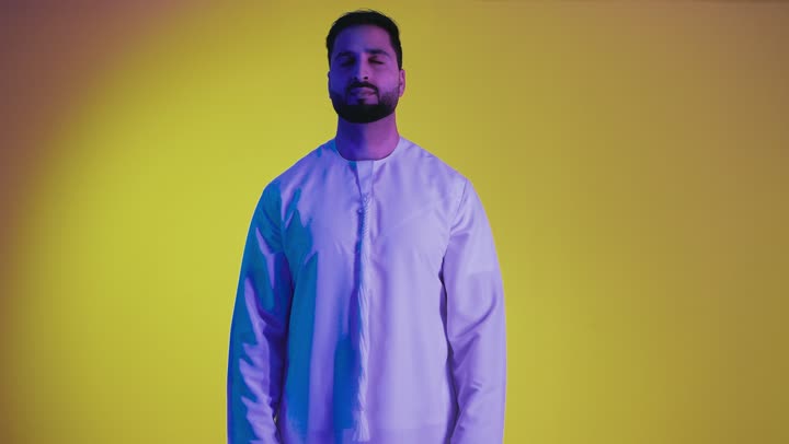 Raising hands with signs of quality and acceptance, excellence and full marks, expressing admiration and appreciation, feeling satisfied and pleased, a picture of an Emirati Gulf Arab man wearing a kandura looking at the camera with gestures of happiness and pleasure, full body, yellow background.
