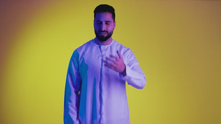 Surprise and shock when seeing something, upset when hearing bad news, falling into a calamity, looking at the camera with an expression of surprise, a picture of an Emirati Gulf Arab man wearing a kandura, putting his hands on his face with an expression of astonishment and amazement, yellow background.