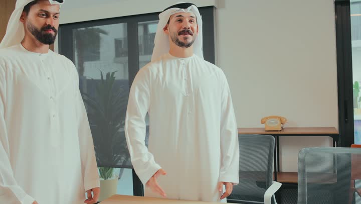 Conducting a job interview and test, a new business agreement between partners, a successful joint group deal, presenting ideas and solutions, two Emirati Arab businessmen wearing kandora and ghutra shaking hands with a young man wearing a formal suit in the meeting room, greeting, greeting and getting to know each other, exchanging information and experiences