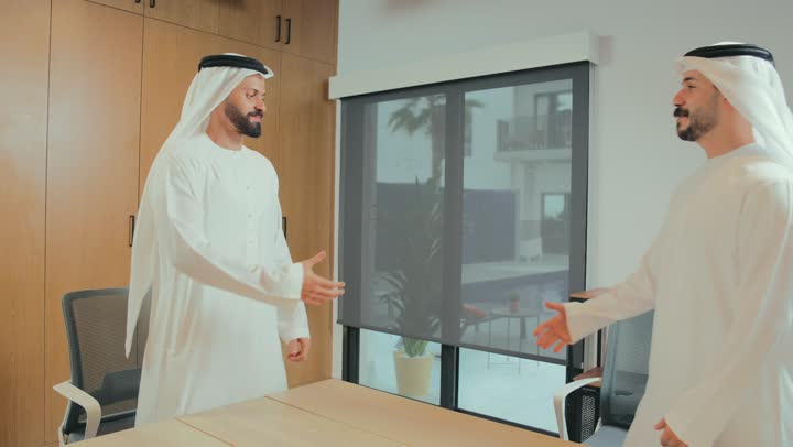 إجراء مقابلة توظيف واختبار، اتفاقية عمل جديده بين الشركاء، صفقة جماعية مشتركة ناجحة، تقديم الافكار والحلول، رجلا اعمال عربيان خليجيان اماراتيان يرتديان الكندورة والغترة يتصافحان بإيماءات السرور في غرفة الاجتماعات، التحيه والسلام والتعارف، تبادل المعلومات والخبرات