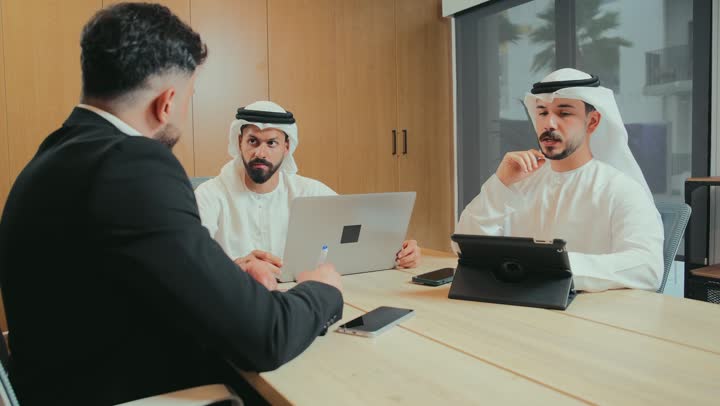 Understanding and cooperation among colleagues to achieve company goals, a comfortable work environment in Emirati companies, the use of modern technical devices in offices, dialogue and discussion to achieve strategies and goals, a business meeting between Arab Gulf and Emirati employees in the conference room, signing a contract and a new deal.