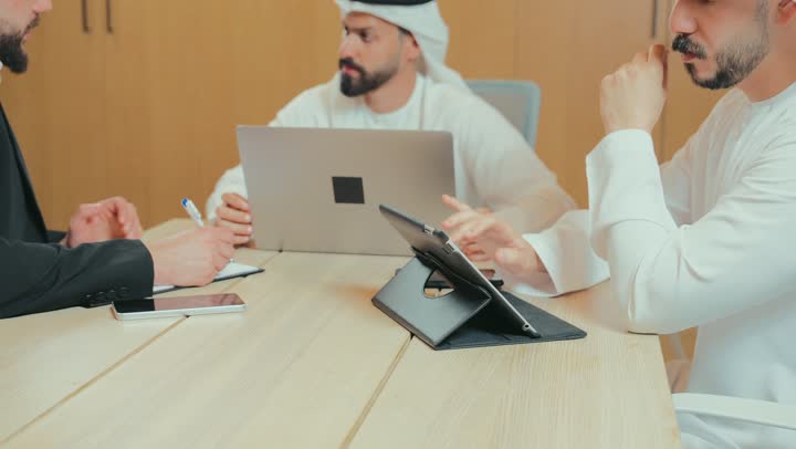 التفاهم والتعاون بين الزملاء لتحقيق أهداف الشركة, بيئة العمل المريحة في الشركات الإماراتية, استخدام الأجهزة التقنية الحديثة في المكاتب, حوار ونقاش لتحقيق الاستراتيجيات والغايات, اجتماع عمل بين موظفين عرب خليجيين اماراتيين في غرفة الاجتماعات، توقيع عقد وصفقة جديدة