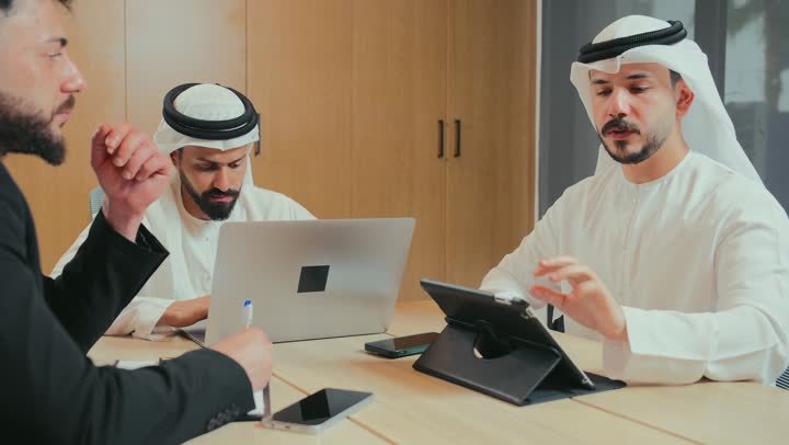 حوار ونقاش لتحقيق الاستراتيجيات والغايات, التفاهم والتعاون بين الزملاء لتحقيق أهداف الشركة, بيئة العمل المريحة في الشركات الإماراتية, استخدام الأجهزة التقنية الحديثة في المكاتب, اجتماع عمل بين موظفين عرب خليجيين اماراتيين في غرفة الاجتماعات، توقيع عقد وصفقة جديدة