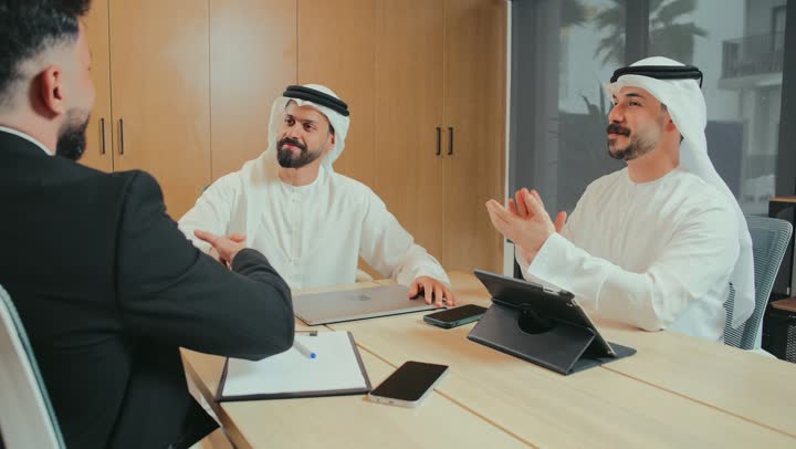 استخدام الأجهزة التقنية الحديثة في المكاتب، حوارات ومناقشات لتحقيق الاستراتيجيات والغايات، اجتماع عمل بين موظفين عرب خليجيين إماراتيين في غرفة الاجتماعات، تعابير المصافحة والاتفاقيات الجديدة، التفاهم والتعاون بين الزملاء لتحقيق أهداف الشركة
