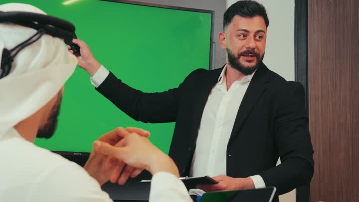 عرض شاشة كروما خضراء فارغة, دمج الأجهزة التقنية الحديثة بالأعمال لسهولة توصيل المعلومة، إدارة و تقسيم المهام، رجل عربي خليجي إماراتي يقوم بشرح المشروع داخل غرفة الاجتماعات للموظفين، فريق عمل يقوم بإجراء اجتماع لتطوير المشاريع و الاستثمارات في الشركة