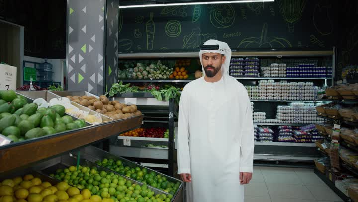 Having a good time at the mall, close-up of an Emirati Gulf Arab man wearing a white kandura picking green apples while shopping in a supermarket, buying consumer needs and household items, various goods and food items