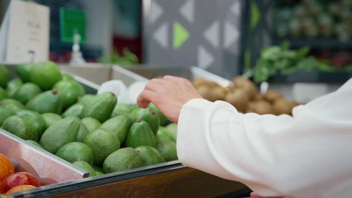 Displaying products and food items on the shelves in the store, enjoying shopping in the fruit section inside the supermarket, a close-up of an Emirati Gulf Arab man wearing a white kandura selecting fresh pears, local Emirati agricultural products