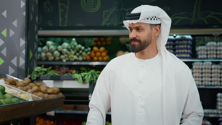 قضاء وقت ممتع في المركز التجاري, صورة مقربة لرجل عربي خليجي اماراتي يرتدي الكندورة البيضاء يقوم بانتقاء التفاح الاخضر أثناء تسوقه داخل أحد السوبرماركت , شراء الاحتياجات والمستلزمات المنزلية للمستهلك, السلع والمواد الغذائية المختلفة