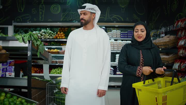 الإستمتاع بالشراء والتبضع مع الأهل، التعاون الأسري والاهتمام بشراء الأغذية الطازجة، زوجان عربيان خليجيان اماراتيان يرتديان الزي التقليدي يقومان بالتسوق و انتقاء التفاح الاخضر في السوبرماركت ، محاصيل زراعيه وطنية اماراتية، السلع والمواد الغذائية المختلفة