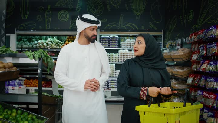 Healthy and beneficial foods, sharing in purchasing household necessities, an Emirati Gulf Arab couple wearing traditional dress choosing fresh green apples from the supermarket, Emirati national agricultural crops