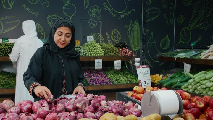 شراء الاحتياجات المنزلية، زوجان عربيان خليجان امارتيان يرتديان الزي التقليدي يقومان بالتبضع وانتقاء البصل الاحمر الطازج،المشاركة في شراء اللوازم المنزلية، قسم الخضراوات والفواكه الطازجه في السوبر ماركت، محاصيل زراعيه اماراتية