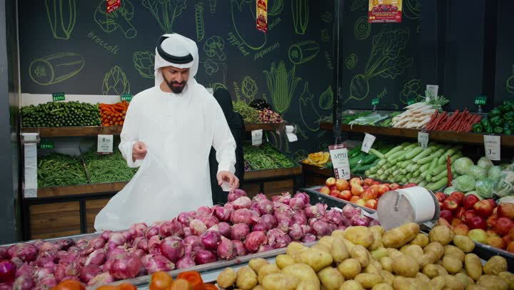 Shopping and choosing fresh vegetables in the supermarket, taking advantage of the offers and discounts on food products, an Emirati Gulf Arab man wearing a white kandura selecting fresh onions, nutritional awareness and attention to detail while shopping, a local Emirati product