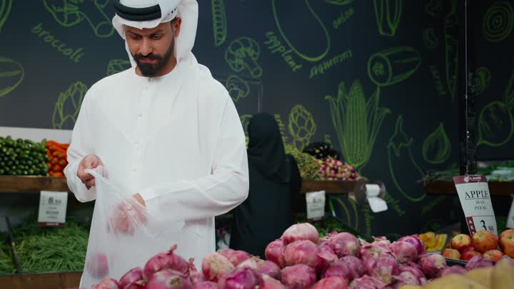 الإستفادة من العرض و التخفيض على السلع الغذائية، التبضع واختيارالخضار الطازج داخل السوبرماركت، رجل عربي خليجي إماراتي يرتدي الكندورة البيضاء يقوم بانتقاء البصل الطازج، الوعي الغذائي والاهتمام بالتفاصيل أثناء التسوق، منتج محلي وطني اماراتي