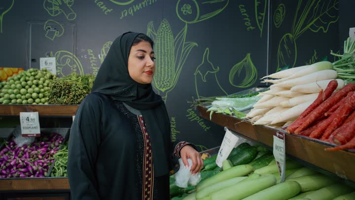 Buying products from the supermarket, strolling around the mall, an Arab Gulf Emirati couple sharing in buying household supplies, taking advantage of discounts and offers, a local Emirati product, an Arab woman selecting fresh eggplant