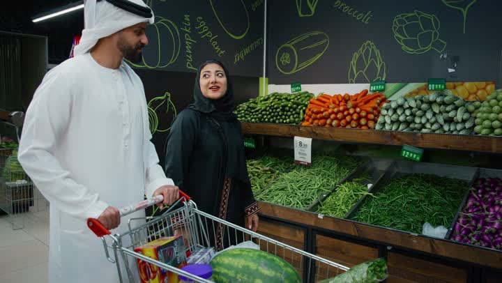 اختيار السلع والمواد الغذائية المختلفة، التعاون والتشاور في شراء بعض المستلزمات والحاجات الضرورية، الاستمتاع بالتسوق مع العائلة في المول, زوجان عربيان اماراتيان خليجيان يقومان بالتسوق فى السوبرماركت، امراة عربية تقوم بانتقاء الباذنجان الطازج، متعة الشراء والتسوق في الامارات