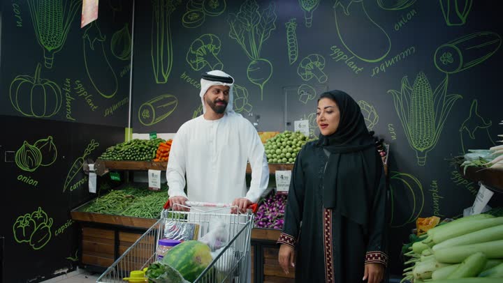 التعاون والتشاور في شراء بعض المستلزمات والحاجات الضرورية، اختيار السلع والمواد الغذائية المختلفة، الاستمتاع بالتسوق مع العائلة في المول, زوجان عربيان اماراتيان خليجيان يقومان بالتسوق فى السوبرماركت، متعة الشراء والتسوق في الامارات