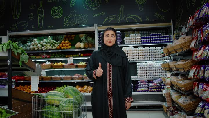 تعابير الرضا والموافقة, شراء الاحتياجات و المستلزمات المنزلية للمستهلك، تصوير لامراة عربية خليجيه اماراتية ترتدي العباءه السوداء تشير باصبعها الابهام الى الاعلى، ايماءات وجه ويدين تدل على الموافقة والقبول، سيده سعوديه تقوم بالتسوق داخل السوبرماركت