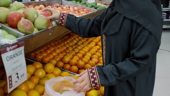 البحث عن أجود وأفضل أنواع الخضراوات والفواكه داخل السوبرماركت، منتج محلي وطني سعودي, شراء الاحتياجات و المستلزمات المنزلية للمستهلك، تصويرمقرب لامراة عربية خليجيه اماراتية ترتدي العباءه السوداء تقوم بانتقاء المانجو، سيده سعوديه تقوم باختيار أجود المنتجات من المركز التجاري