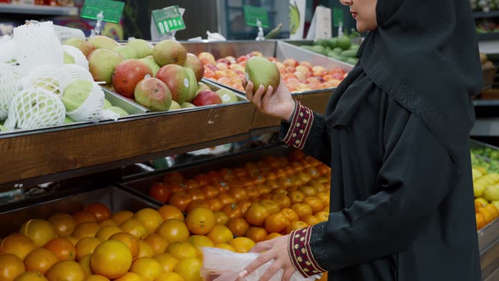 متعة التسوق وشراء السلع المختلفة، منتج محلي وطني سعودي, شراء الاحتياجات و المستلزمات المنزلية للمستهلك، تصويرمقرب لامراة عربية خليجيه اماراتية ترتدي العباءه السوداء تقوم بانتقاء المانجو، سيده سعوديه تقوم باختيار أجود المنتجات من المركز التجاري