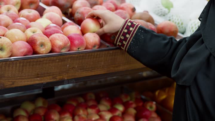 الإستفادة من العرض و التخفيض على السلع الغذائية، منتج محلي وطني سعودي, قضاء وقت ممتع في التسوق, شراء الاحتياجات و المستلزمات المنزلية للمستهلك، تصويرمقرب ليد امراة خليجيه اماراتية ترتدي العباءه السوداء تقوم بانتقاء التفاح، سيده سعوديه تقوم باختيار أجود المنتجات من المركز التجاري