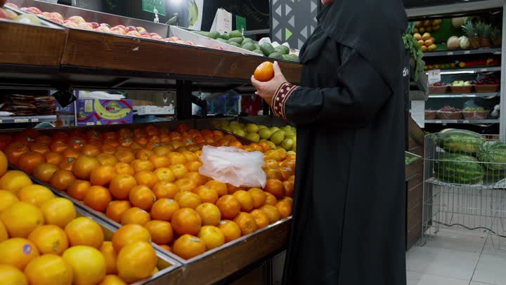 التمتع بالتخفيضات والعروض والخصومات على المنتجات, منتج محلي وطني سعودي, قضاء وقت ممتع في التسوق, شراء الاحتياجات و المستلزمات المنزلية للمستهلك، تصوير لامراة خليجيه اماراتية ترتدي العباءه السوداء تقوم بانتقاء البرتقال، سيده سعوديه تقوم باختيار أجود المنتجات من المركز التجاري