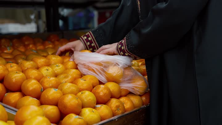 منتج محلي وطني سعودي, قضاء وقت ممتع في التسوق, شراء الاحتياجات و المستلزمات المنزلية للمستهلك، تصوير مقرب ليد امراةعربيه خليجيه اماراتية ترتدي العباءه السوداء تقوم بانتقاء البرتقال، سيده سعوديه تقوم باختيار أجود المنتجات من المركز التجاري