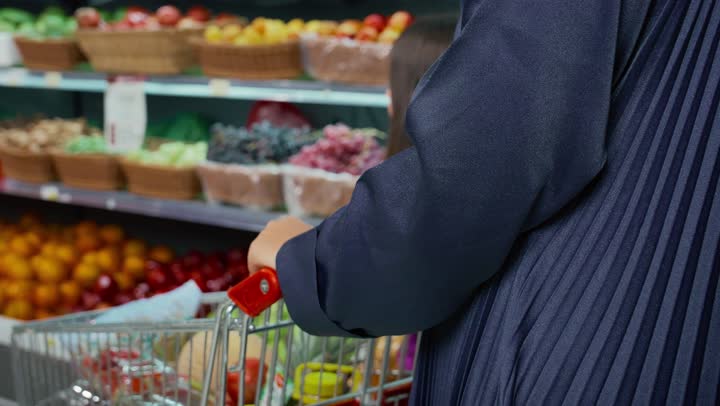 مشاركة البنات في التبضع من متجر المواد الغذائيه، تعليم الأطفال على التسوق، الإشاره إلى المنتج الأفضل، امرأه عربيه خليجيه سعوديه ترتدي العباءه الرماديه وتقوم بالتبضع مع ابنتها، سيده اماراتيه تقوم بشراء ثمره الرمان مع ابنتها، منتج محلى اماراتي