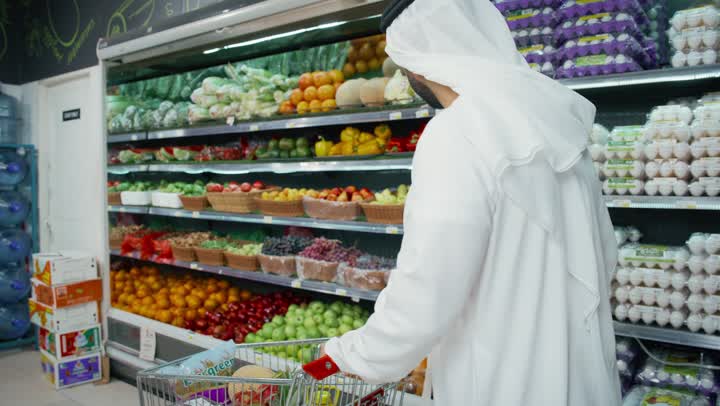 التبضع والتسوق في السوبر ماركت, قضاء وقت ممتع في التبضع واختيار اللوازم المنزليه,  عربه تسوق مليئه بالخضروات والفاكهه الاماراتيه، رجل عربي خليجي اماراتي يرتدي الكندوره والغتره البيضاء يتجول في أحد أقسام الماركت ويمسك عربة التسوق، منتجات محليه وطنيه