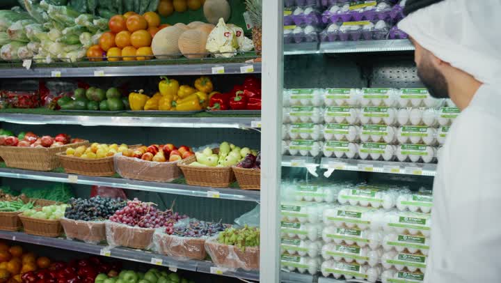 An Emirati Gulf Arab man wearing a white kandura and ghutra inspecting yellow peppers before buying, a gesture of dissatisfaction with the quality of the product, shopping in the supermarket, local national products